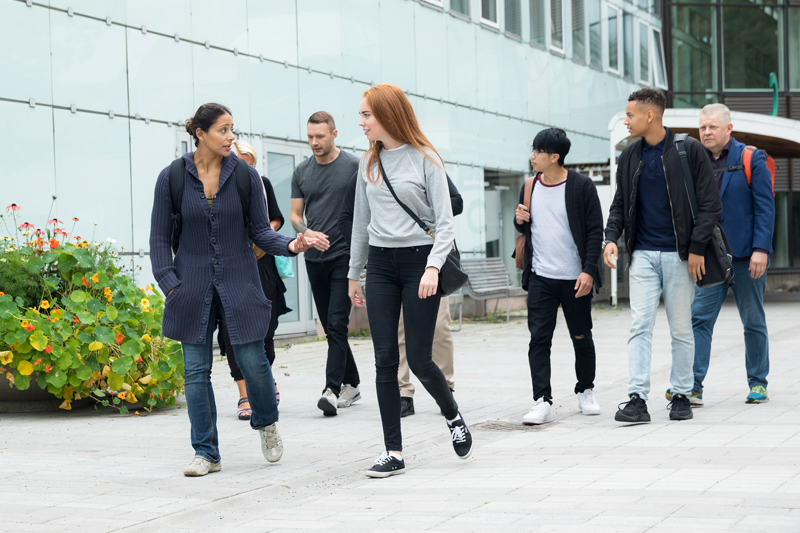 Två unga kvinnor går framför en universitetsbyggnad och diskuterar.